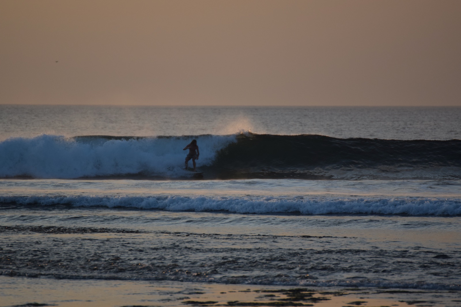Surfeur sur une vague au coucher du soleil à Balangan
