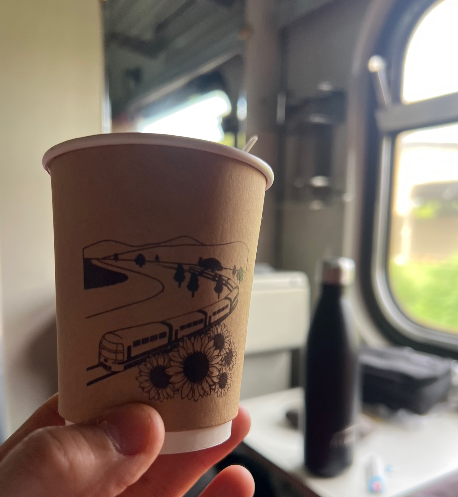 Gobelet de café tenu devant la fenêtre du train