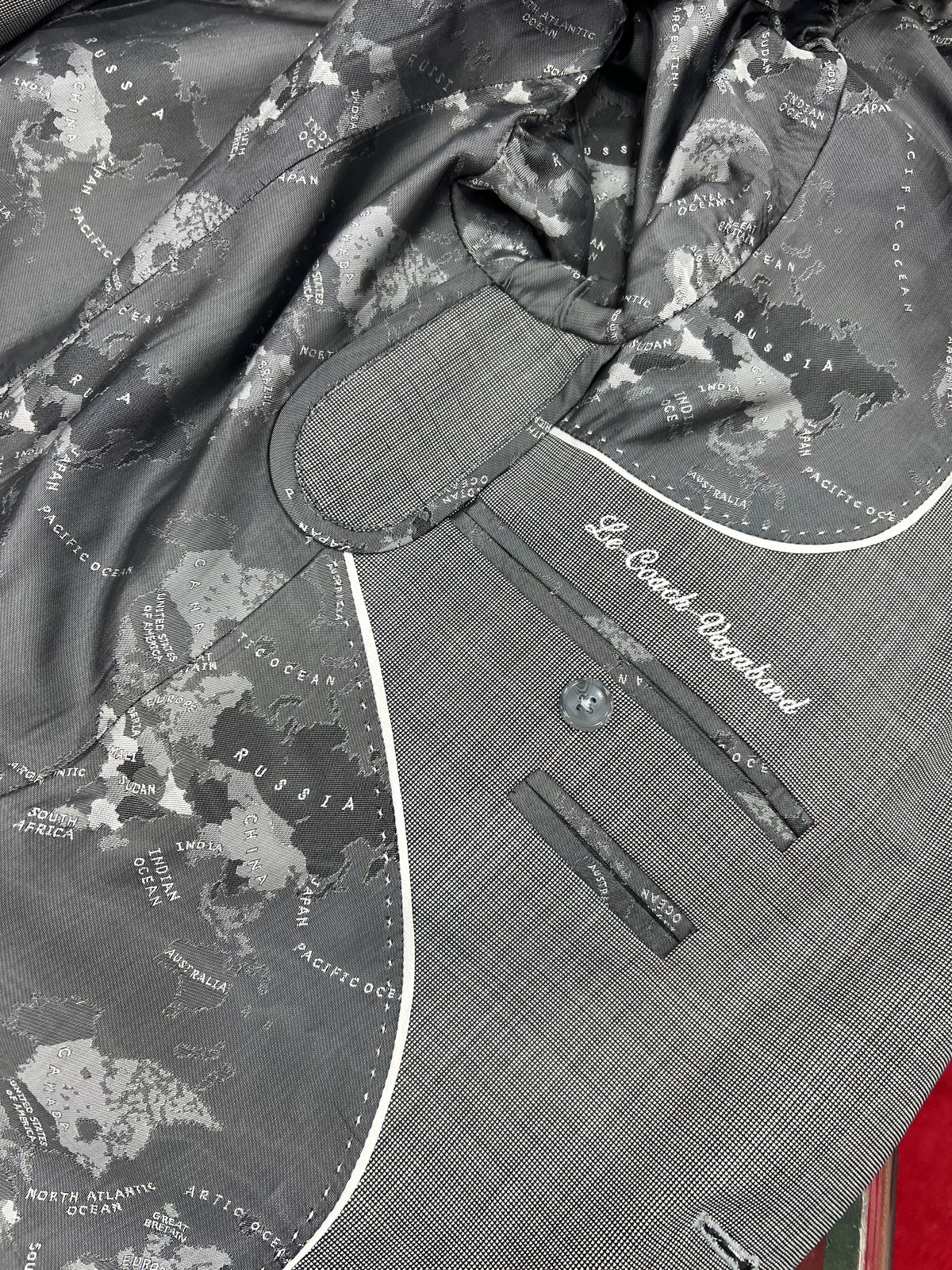Doublure imprimée d'une mappemonde et brodée « Le Coach Vagabond » dans un costume sur mesure gris
