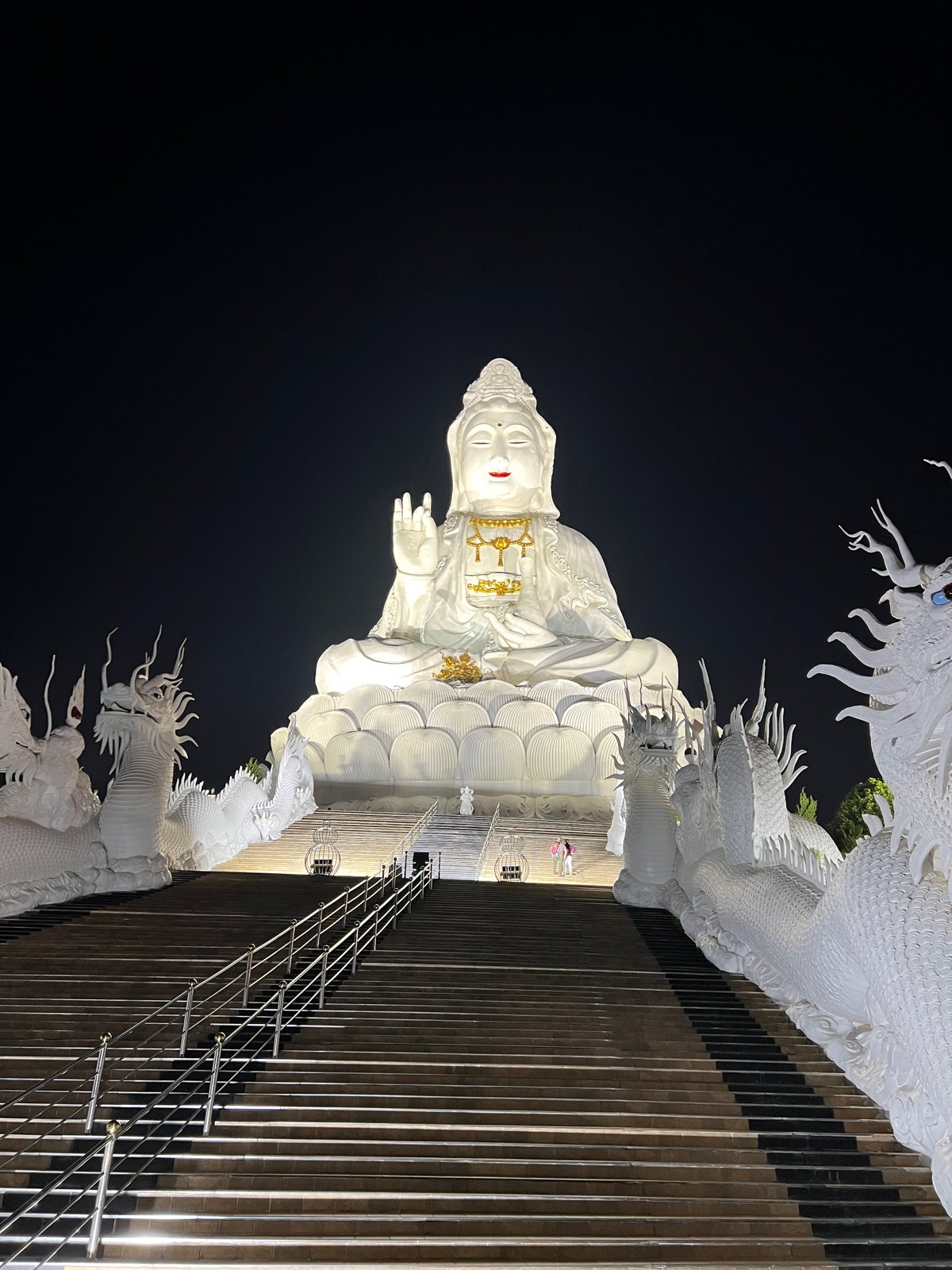 Grande statue blanche de Guanyin au sommet d'un escalier, la nuit
