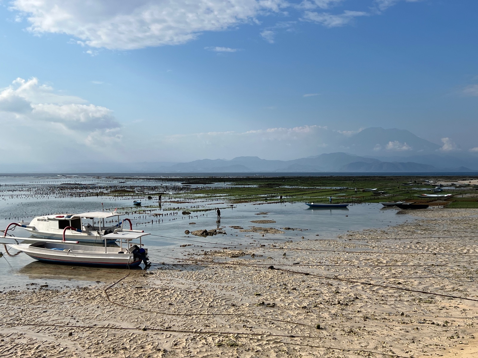 Plage à marée basse à Nusa Lembongan avec un bateau et les volcans de Bali au loin