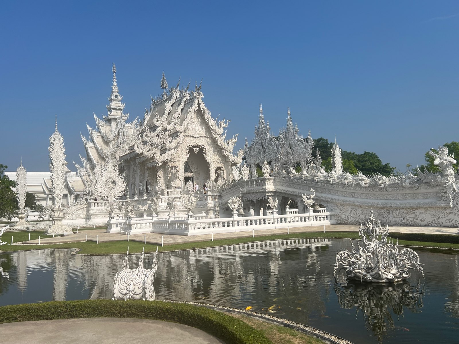Le Temple blanc de Chiang Rai et son bassin sous un ciel bleu