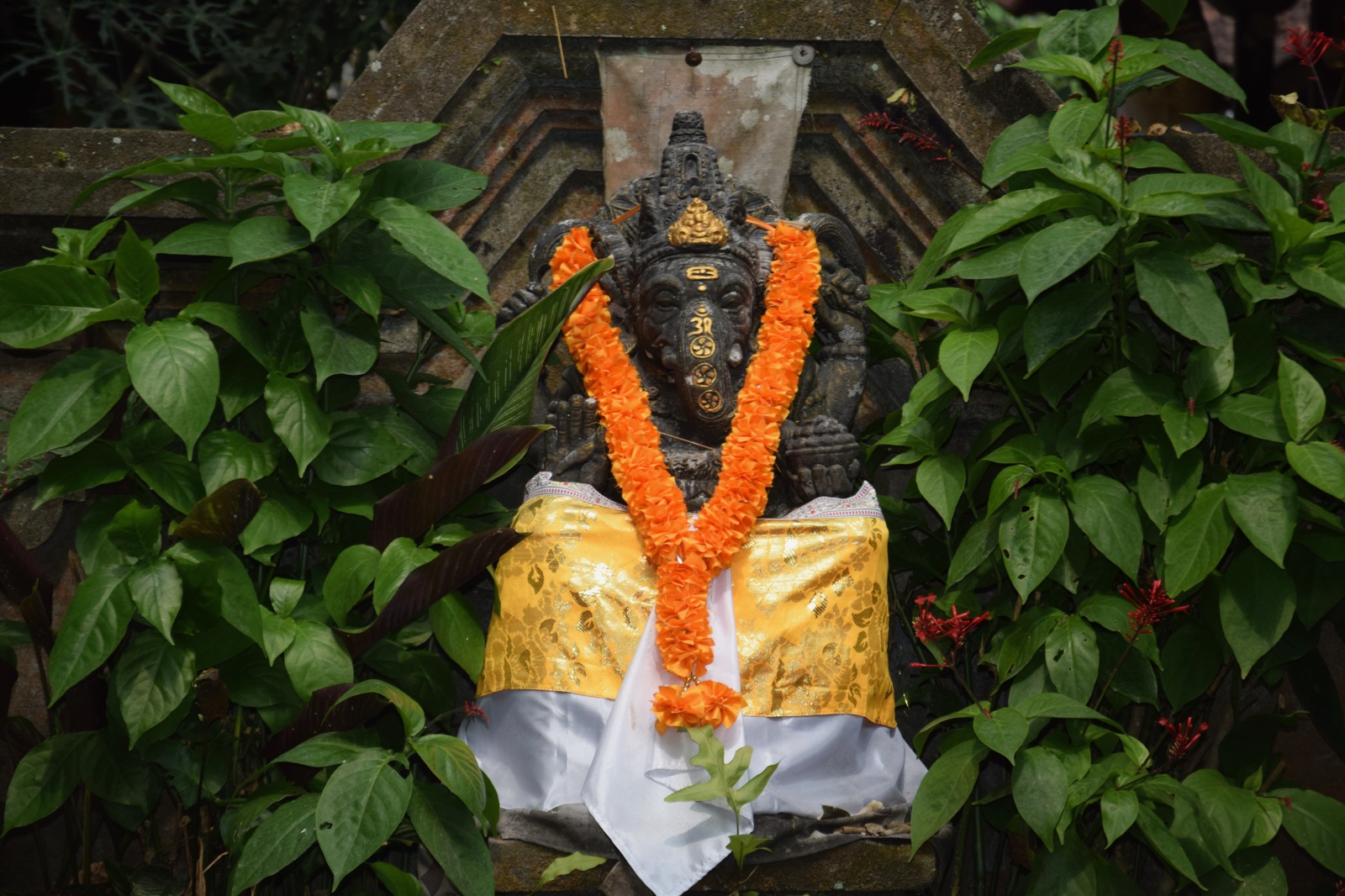 Statue ornée d'un collier de fleurs orange et d'un tissu jaune et blanc à Ubud
